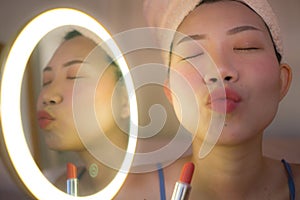 Pretty Asian woman cleaning her face - lifestyle portrait of young happy and beautiful Chinese girl at home applying makeup and