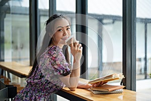 A pretty Asian woman in a cute dress is enjoying her coffee in a coffee shop on the weekend