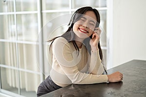A pretty Asian woman enjoys listening to music through her headphones while sitting at a table