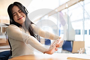 A pretty Asian woman enjoys the music and stretches her arms while relaxing at a table