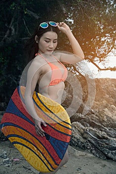 Pretty Asian woman in orange bikini holding a surf board on the beach.