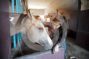 Pretty Asian woman petting horse in a farm.