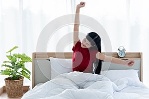 Pretty Asian woman is sitting on a clean white bed, stretching her arms to muscle relaxation After she woke up