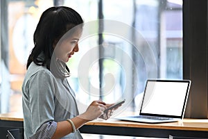 Pretty asian woman sitting in front of laptop and using smart phone.