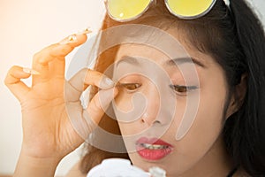 Pretty Asian woman sticks false eyelashes of herself.