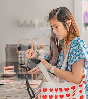 Pretty Asian woman taking out card and cash to pay at cafe restuarant at the counter