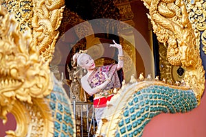 Pretty Asian woman wear Thai traditional dress stand and action of Thai dance in front of door of temple and naga sculpture as