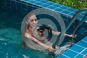 Pretty Asian woman wearing red bikini swim and standing at stair at swimming pool.