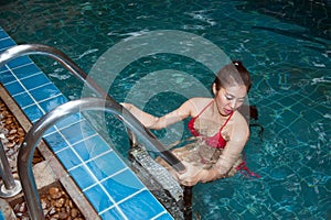 Pretty Asian woman wearing red bikini swim and standing at stair at swimming pool.