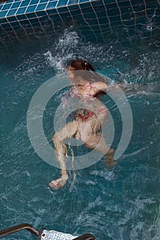 Pretty Asian woman wearing red bikini swimming on back at swimming pool and enjoying on water.