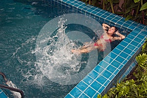 Pretty Asian woman wearing red bikini swimming on back at swimming pool and enjoying on water.