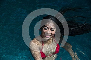 Pretty Asian woman wearing red bikini swimming at swimming pool and enjoying travel on vacation summer time.