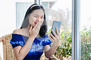 Pretty Asian young woman holding smartphone using mobile phone app for video call, laughing while watching funny video