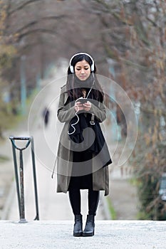 Pretty asian young woman listening to music with her smartphone in the street.