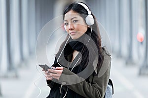 Pretty asian young woman listening to music and looking at camera in the street.