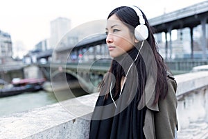 Pretty asian young woman listening to music and looking sideways in the street.