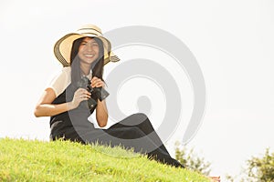 Pretty Asian young woman sit on mound seeking binoculars .