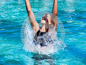 Pretty athletic sun tanned girl splashing in a swimming pool on vacation