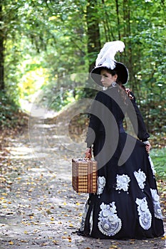 Girl in retro dress 18th century with valise in park