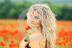 Pretty attractive lady with blond curly hair that fell on her face, in a beautiful red poppy field, turns to the camera