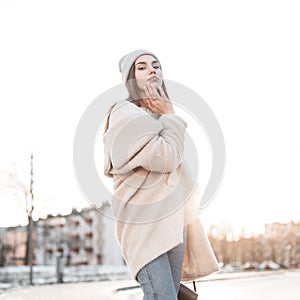 Pretty attractive stylish young woman in a fashion winter fur coat made of faux fur in a knitted trendy hat enjoys the bright
