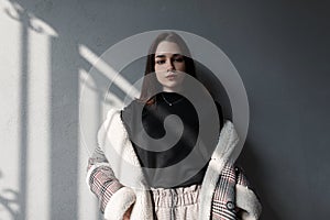 Pretty attractive young woman fashion model brunette in a fashionable jacket in vintage pants is standing in a gray studio