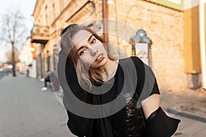 Pretty attractive young woman with natural make-up with sexy lips in fashionable clothes poses outdoors near brick vintage houses