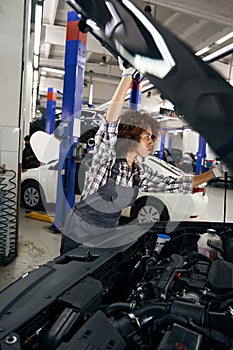 Pretty auto repair shop employee lifts car hood