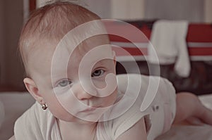 Pretty baby girl crawling on the bed. Cute toddler girl lies on the bed smiling. 6 months old baby girl. Portrait of a