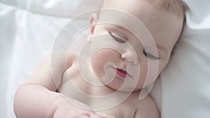 Pretty baby girl drinks milk from bottle lying on bed. Child weared diaper in nursery room.