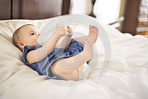Pretty baby girl drinks water from bottle lying on bed