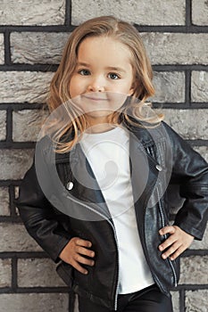 Pretty baby girl in fashion outfit: white t-shirt, leather black jacket and leggings