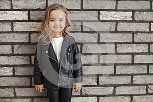 Pretty baby girl in fashion outfit: white t-shirt, leather black jacket and leggings