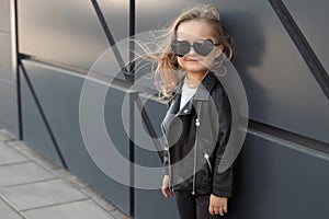 Pretty baby girl in fashion outfit: white t-shirt, leather black jacket and leggings, sunglasses hearts