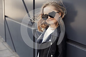 Pretty baby girl in fashion outfit: white t-shirt, leather black jacket and leggings, sunglasses hearts