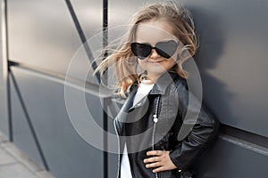 Pretty baby girl in fashion outfit: white t-shirt, leather black jacket and leggings, sunglasses hearts