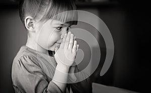 Pretty baby girl praying at home monochrome banner photo. A black-and-white photo of a girl who folded her hands in prayer and sup