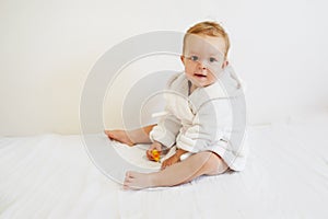 Pretty baby with a white bathrobe after taking a bath sitting on white cover on white background