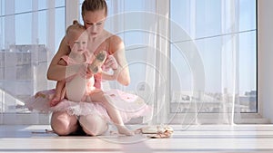 Pretty ballerine teaches her little daughter how to tie ballet pointe shoes