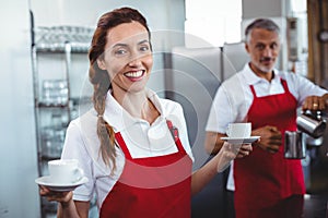 Pretty barista holding cups of coffee with colleague behind