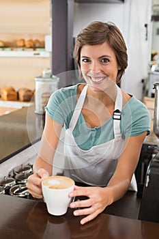 Pretty barista offering cup of coffee smiling at camera