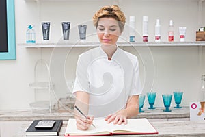 Pretty beautician writing in appointment book