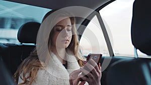 Pretty beautiful blonde with loose hair texting on her phone whilst driving in her modern car from work.