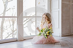 Pretty beautiful girl sitting on the floor with yellow flowers tulips and smiling. Indoor photo. Nice girl. Copy space