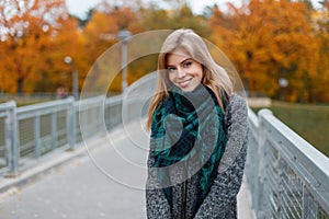 Pretty beautiful young woman with a beautiful smile in a fashionable gray coat with a green vintage scarf walks outdoors