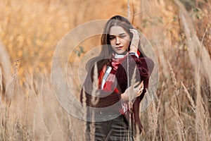 Pretty beautiful young woman model in a knitted vintage sweater with a checkered stylish scarf posing outside the city on an