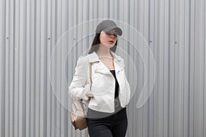 Pretty beautiful young woman with a stylish gold backpack in a fashionable white leather jacket in black jeans