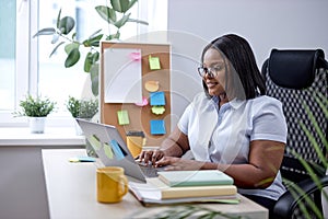 pretty black lady typing on laptop keyboard working online in cozy modern office