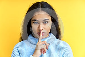 Pretty black woman keeps finger on lips, making hush gesture on yellow background photo
