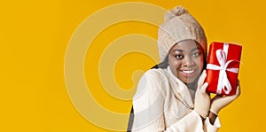 Pretty black woman in winter hat and gloves holding gift